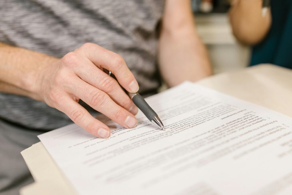 Close-up of a person's hand signing an important legal document with a pen indoors.